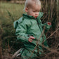 A toddler boy in a waterproof rainsuit on his knees in the wet grass