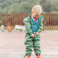 A happy toddler boy in a sage green puddle suit undoing his suit to display his dry clothes underneath