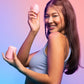 Young woman wearing blue tank top smiling, holding VUSH Plump Palm Vibrator up in right hand and case in left hand.