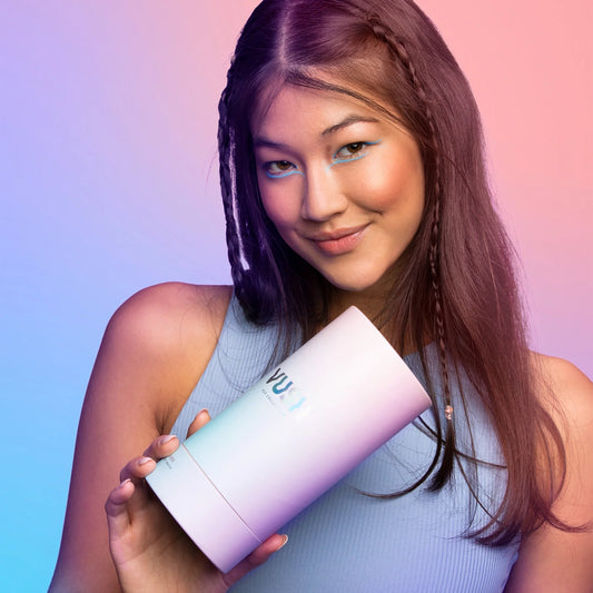 Young woman with long dark hair smiling and wearing a baby blue tank top while holding blue/purple/pink gradient cylinder packaging that reads &quot;VUSH&quot;